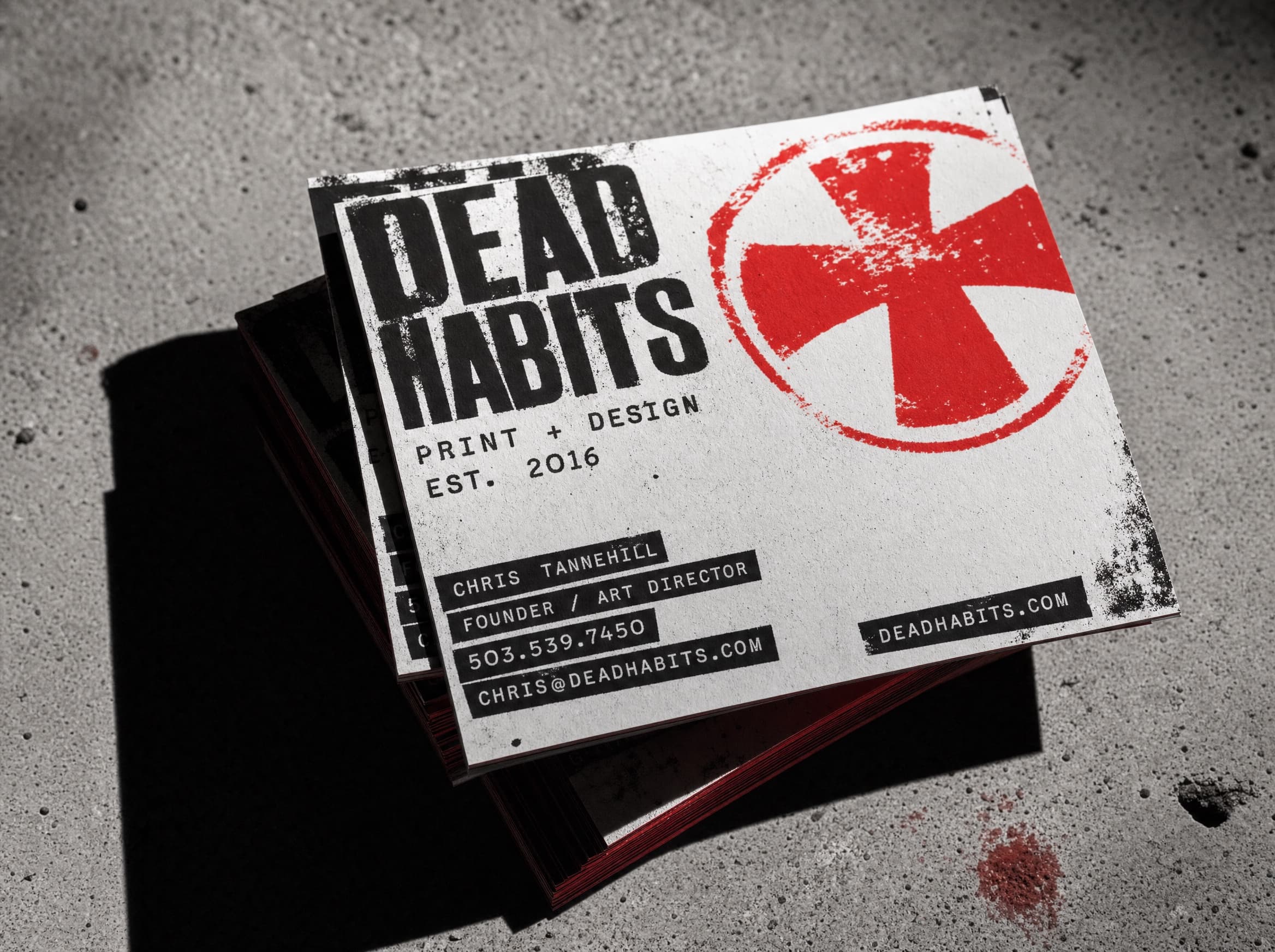 A stack of heavy uncoated business cards on concrete, printed black and red.